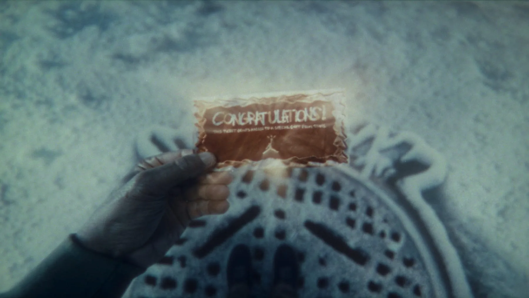 A golden ticket held over a manhole cover in the snow