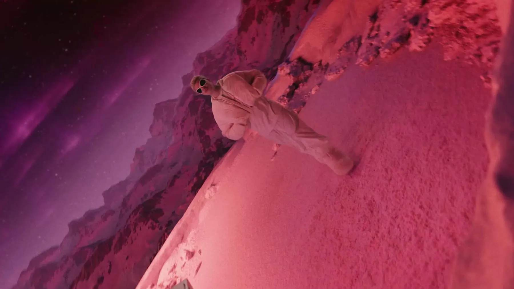 A figure in a white suit crossing a magenta dune
