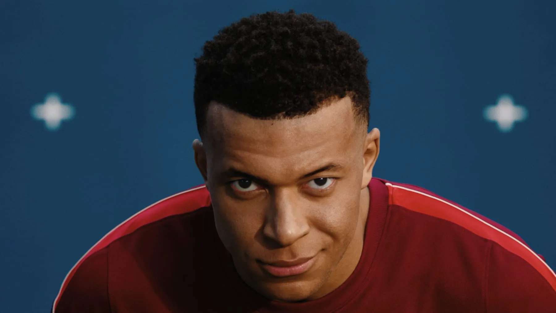 Kylian Mbappé in a red Nike kit, lit against the deep blue stage